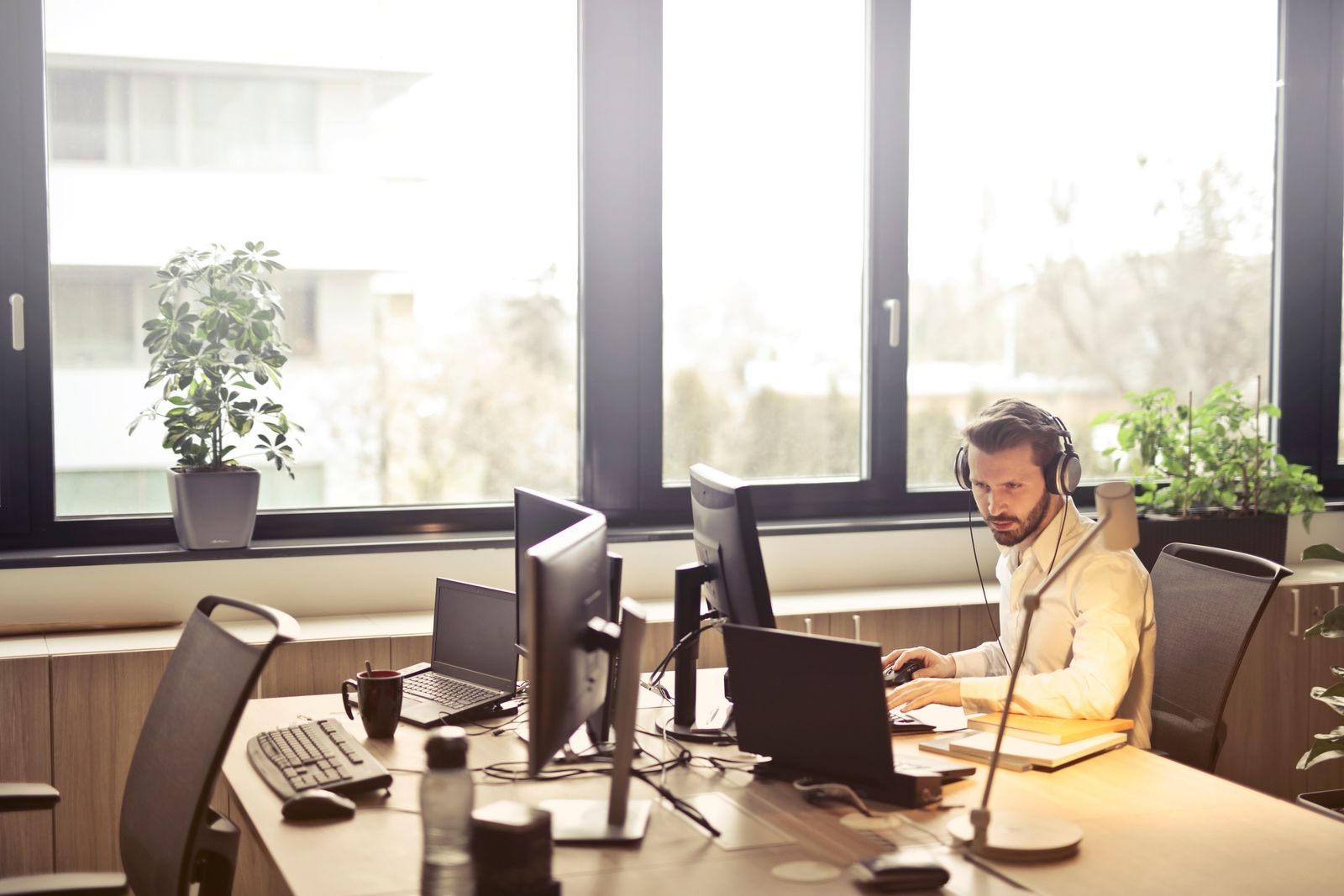A man with a headset working at a desk with several screens